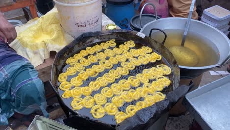 spiral jalebi being cooked in oil at a large pan in a open air market