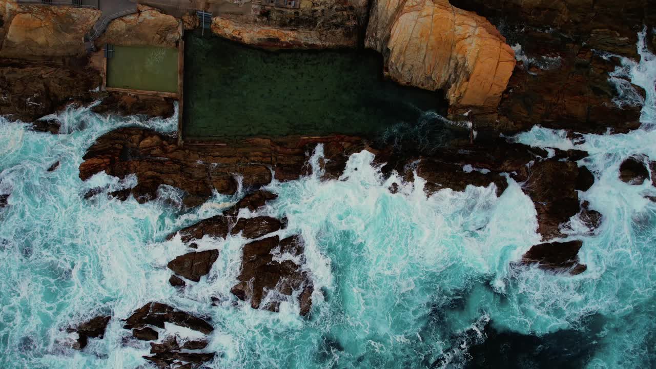 Drone in discesa di onde blu che si infrangono alla Bermagui Blue Pool, Australia
