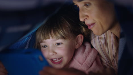 happy mother and daughter using tablet computer under blanket playing games on touchscreen technology relaxing having fun before bedtime