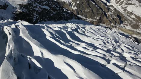 Aerial-view-of-a-mountain-facade-in-the-Swiss-alps-in-winter,-glacier-and-shadows