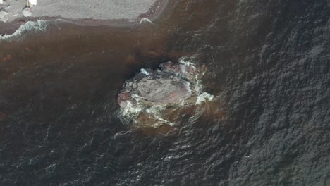 una vista aérea de un avión no tripulado mirando hacia abajo en una pequeña isla rocosa volando sobre el agua y las olas en el lago revelando la playa rocosa de agua dulce del lago superior en minnesota