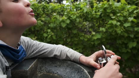feliz joven varón caucásico bebiendo agua dulce del grifo de la fuente al aire libre