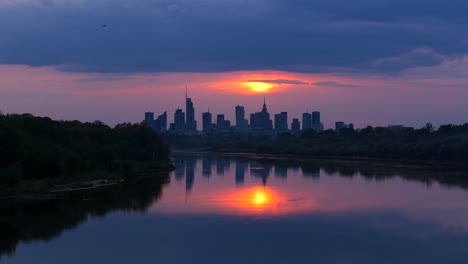 vistula river with downtown district skyscrapers in background at sunset, warsaw, establishing drone shot
