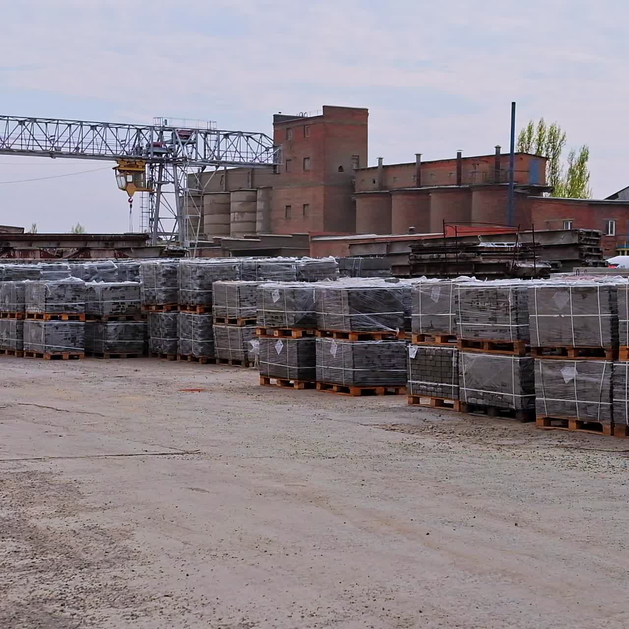 Industrial area with building materials stacked outside. Piles of grey bricks on wooden pallets at the backdrop of plant premises