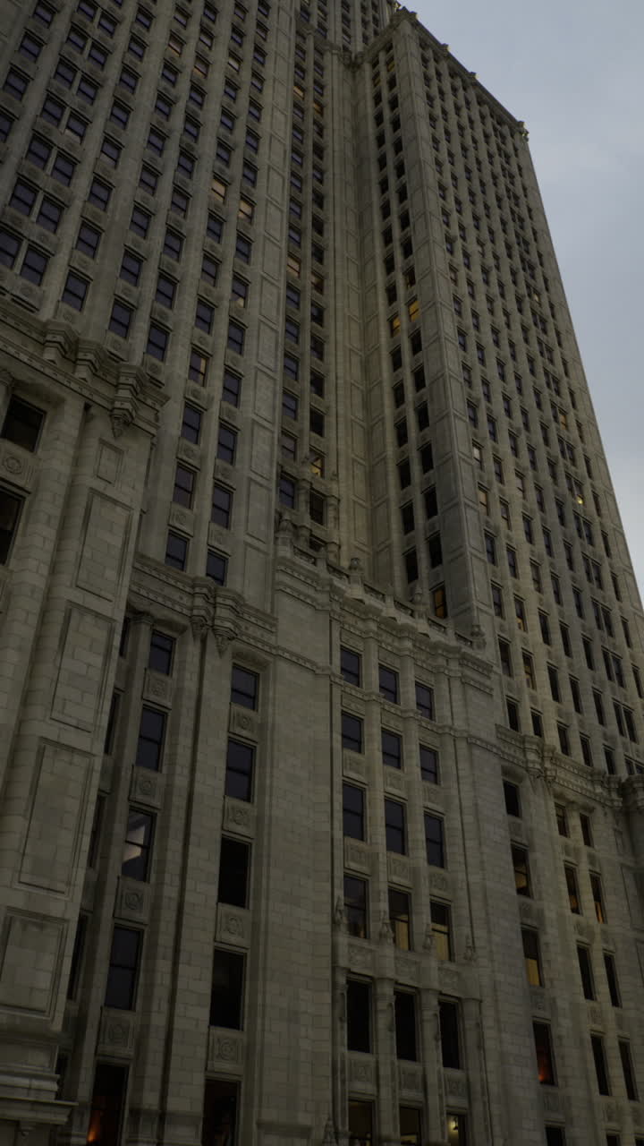 Tall building under a cloudy sky with city lights shimmering at dusk