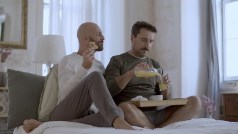 cheerful homosexual men in pajamas having breakfast in bed