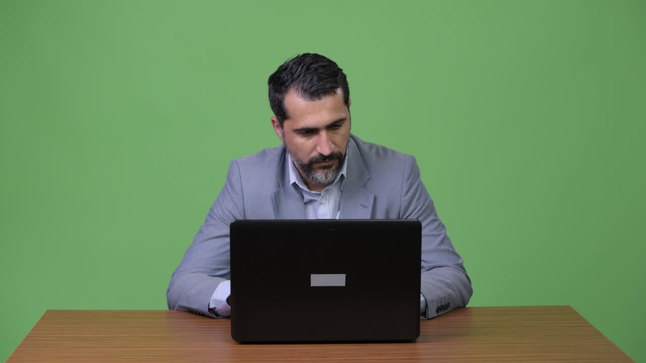 Handsome Persian bearded businessman thinking while using laptop