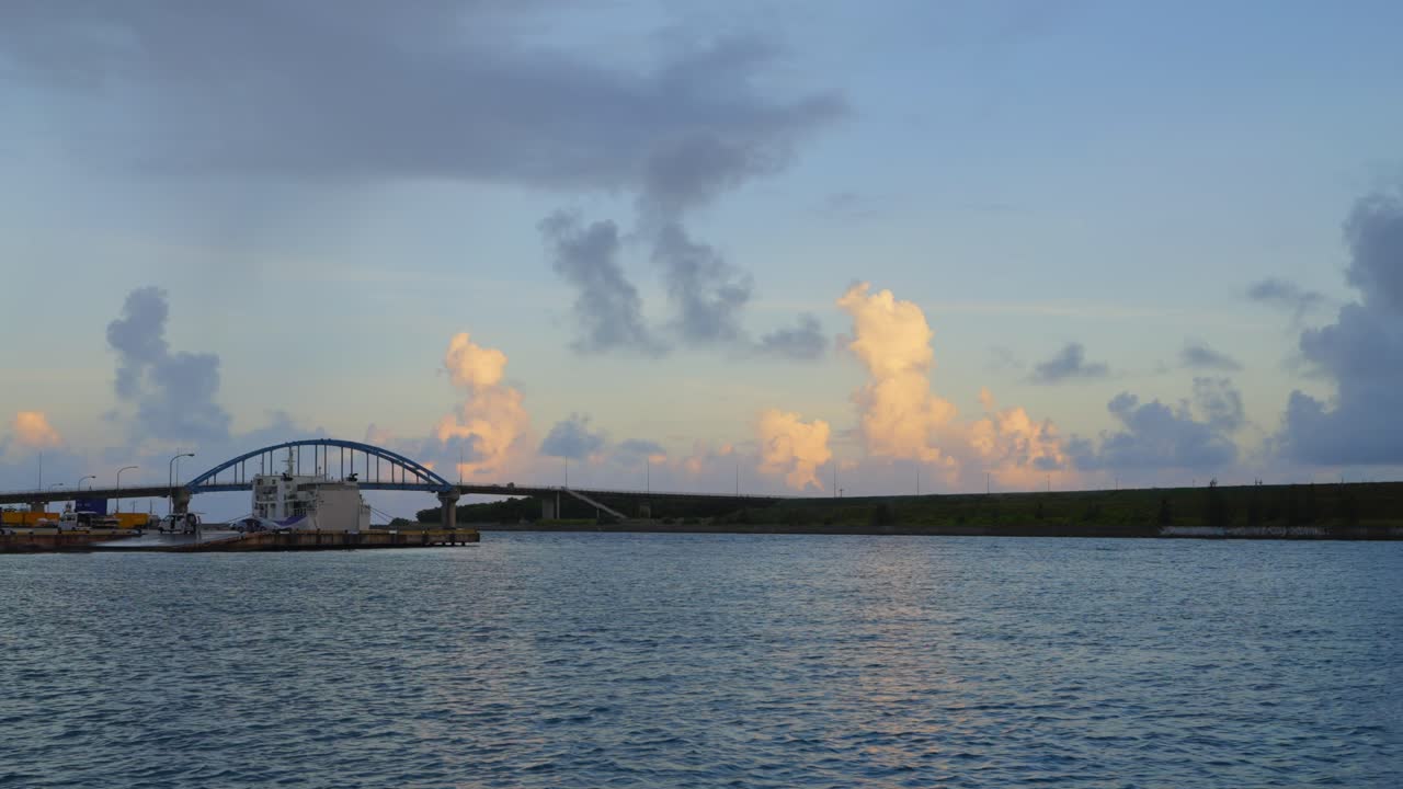From the boat's vantage point, a charming coastal town comes into view, with a bridge silhouetted against sunset-lit clouds