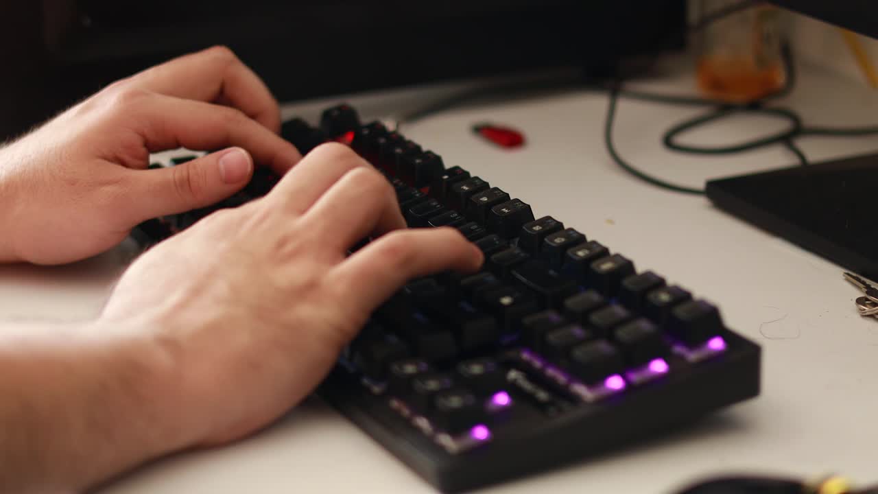 toma en ángulo alto de las manos de un hombre interactuando con un teclado rgb en un escritorio de computadora sucio