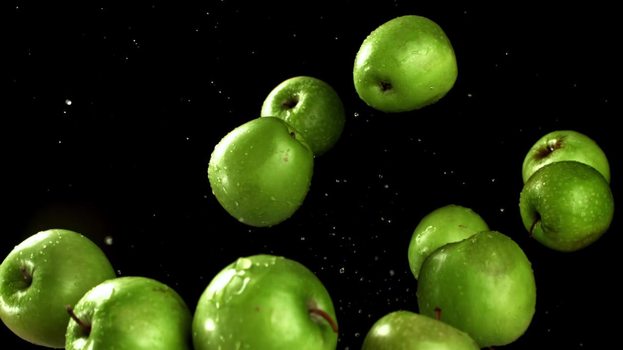 Movimento rallentato di mele verdi con goccioline d'acqua su sfondo nero