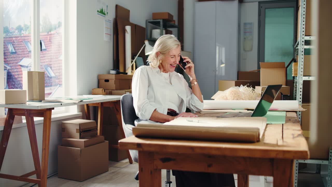 Szczęśliwa starsza bizneswoman rozmawiająca przez telefon i pracująca na laptopie