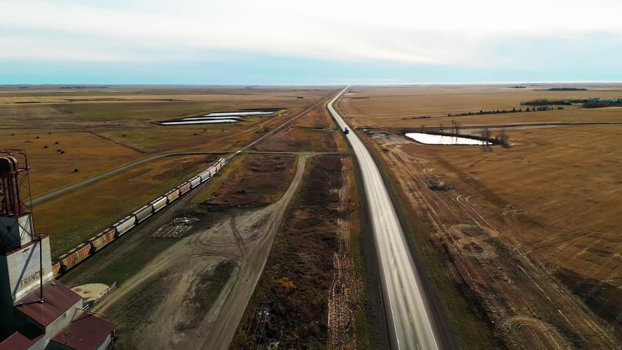 Drone fly over train tracks stretching through rural farmland and main road at Francis, Saskatchewan Province, Canada