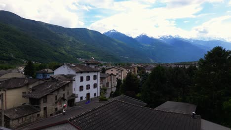 elevated drone view over rooftops of villa di tirano, with snow-covered alps in background and lush valley. captured in villa di tirano, sondrio, italy italia