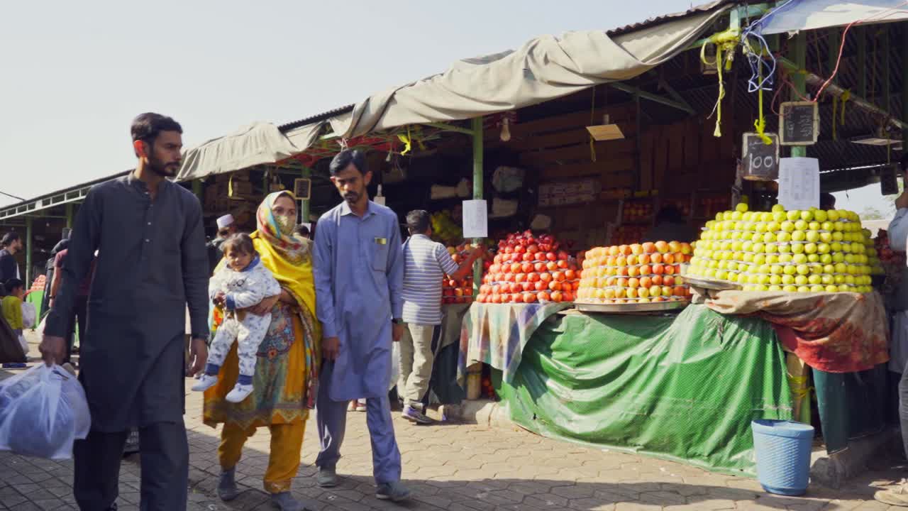 Islamabad market scene featuring people eagerly shopping for a variety of colorful fruits from numerous vendors and stalls.