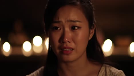 emotional expression: a young woman confronts deep feelings in a dimly lit setting surrounded by flickering candlelight, capturing the essence of vulnerability and reflection