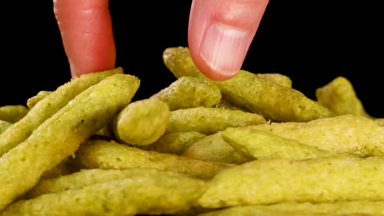 En hånd strekker seg inn i en haug med grønne ertsnacks mot en svart bakgrunn