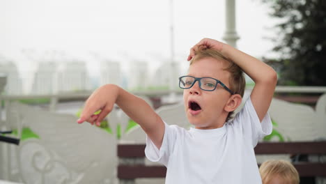 a young boy wearing glasses playfully points at something in the distance while standing outdoors