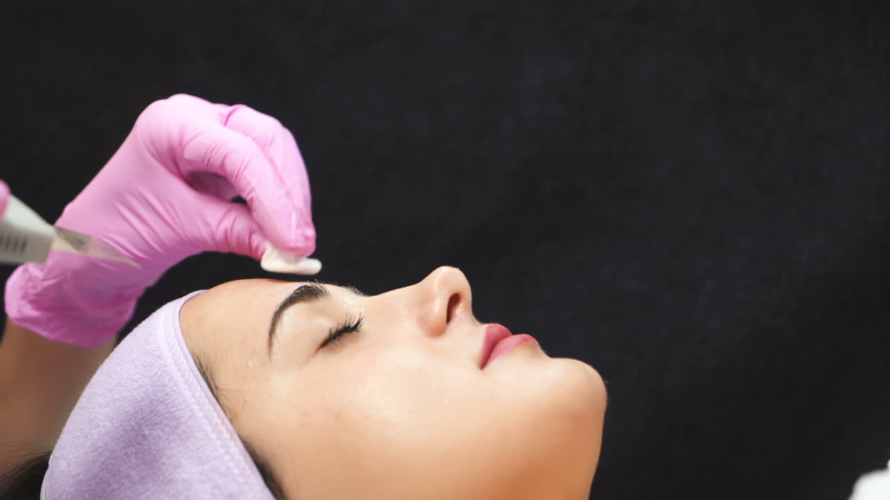 Female cosmetologist using ultrasonic scrubber on client's face. Professional ultrasonic equipment. Face cosmetic procedure.