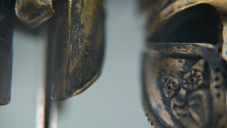 a close-up macro shot of a spartan design, two different ancient warrior metal bronze helmets, textured shapes, studio lighting, full hd cinematic video, hyper slow motion 120 fps, tilt up