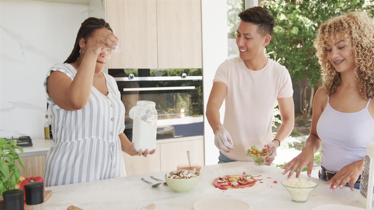 피자를 만들면서 집 주방에서 웃는 아시아인 청년과 종족 여성