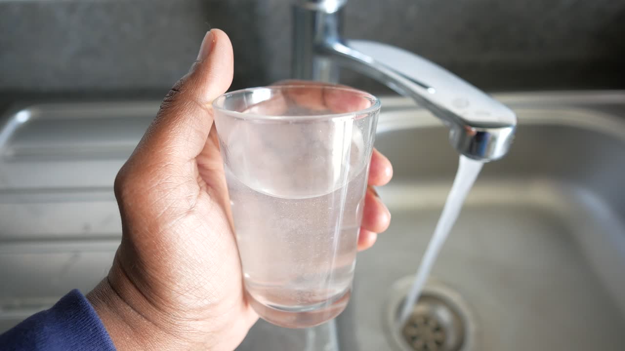 주방 싱크대에서 흐르는  에 물 한 잔을 채우고 있는 손