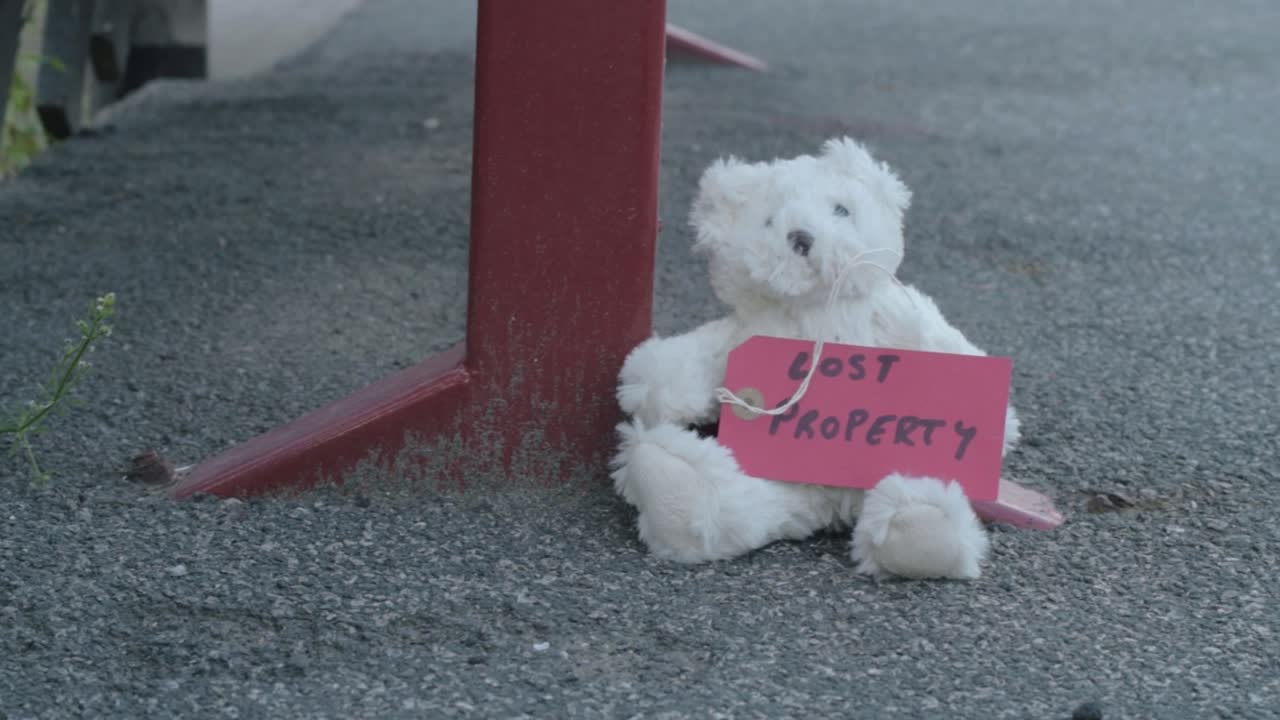 Teddy bear with lost property label left on train platform medium panning shot