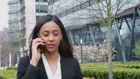 businesswoman commuting to work talking on mobile phone outside modern office building