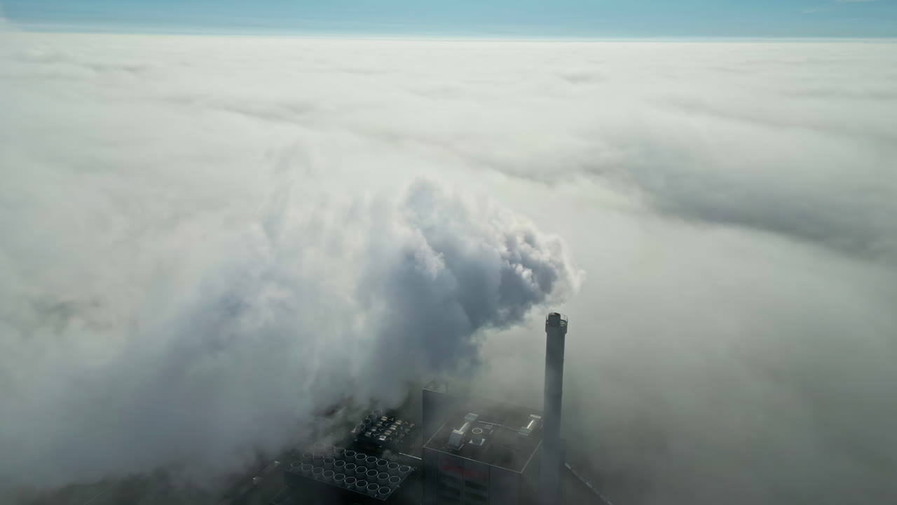 Aerial view of a smoking industrial chimney, in middle of thick low hanging clouds