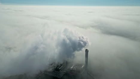aerial view of a smoking industrial chimney, in middle of thick low hanging clouds