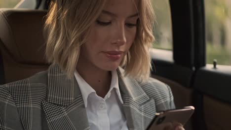 close up view of smiling blonde business woman in coat using smartphone