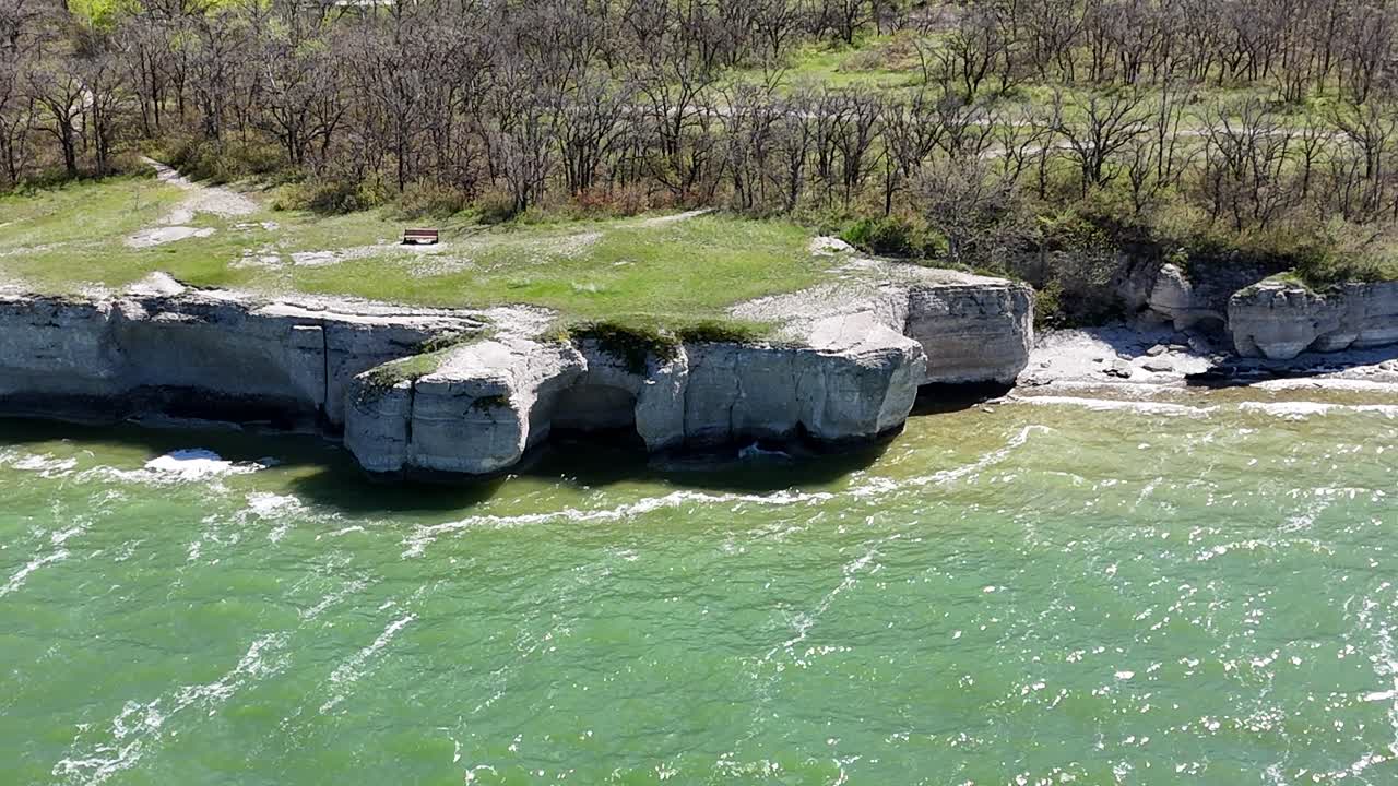 Drone lähenee ja kiertää oikealle Steep Rock Manitoban kalkkikivikallioiden ympärillä, näyttäen Lake Manitoban vihreän veden, rantaviivan ja ympäröivät puut aurinkoisena päivänä.