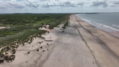 Paraglider-flying-above-sandy-coastline-of-Netherlands,-aerial-drone-view