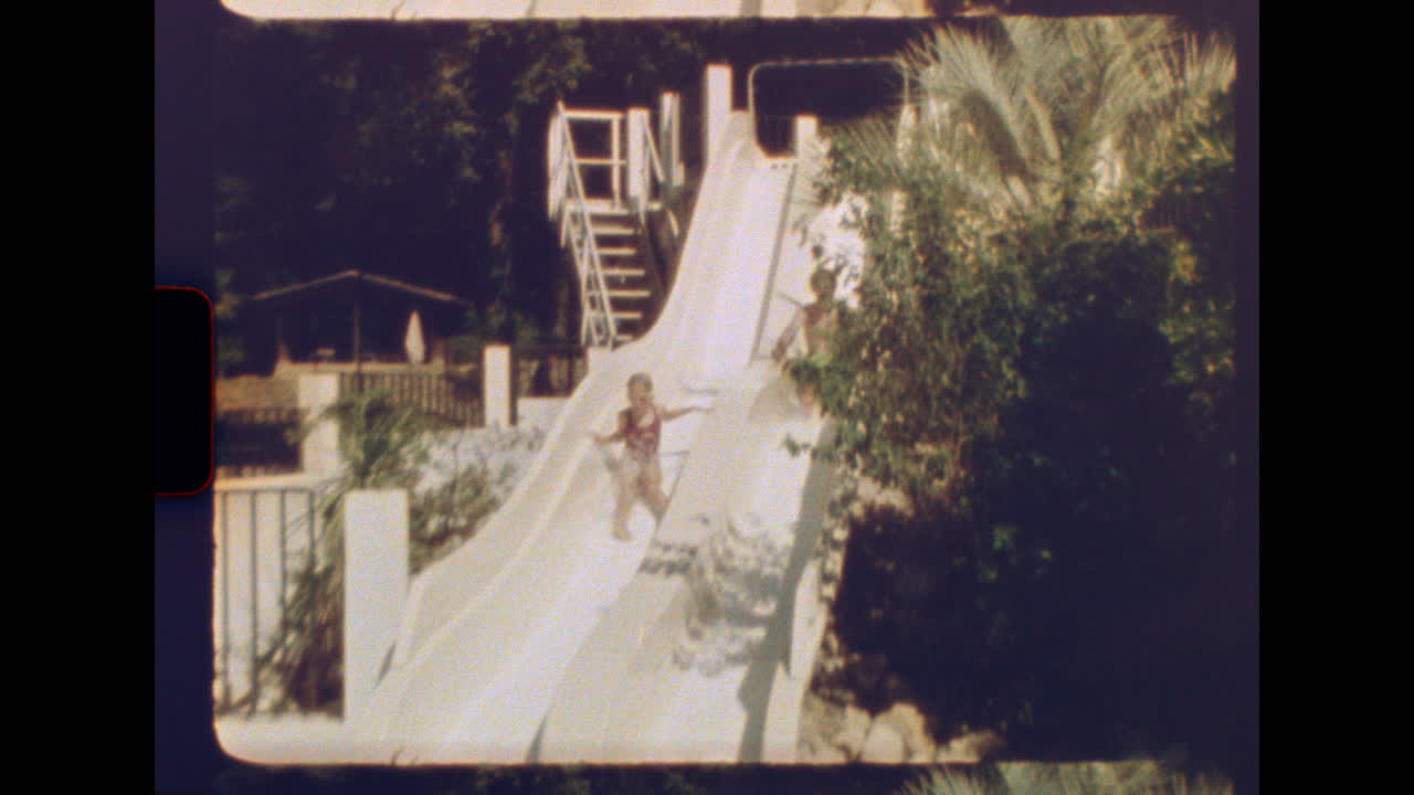 Tonårspojke och unga syster leker på vattenrutschbanor i en retro sommarpool