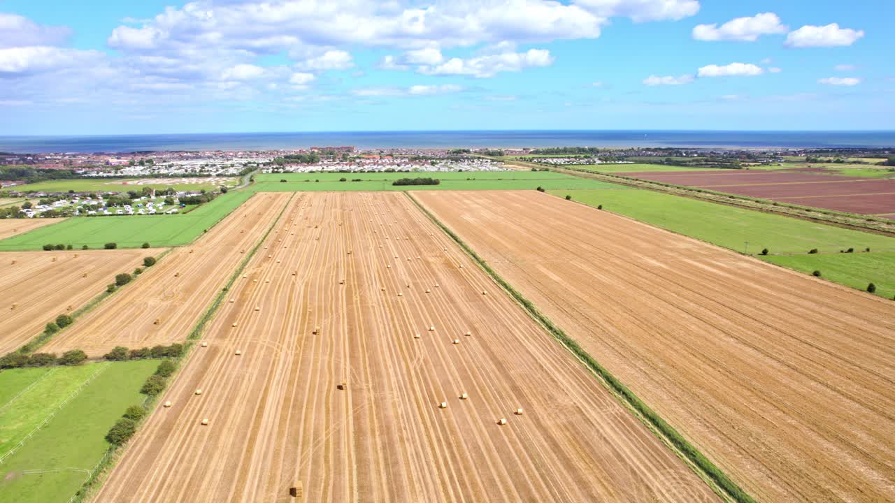 A mesmerizing aerial view captures the wind turbines spinning rhythmically in the Lincolnshire farmer's recently harvested field, with picturesque golden hay bales in the foreground