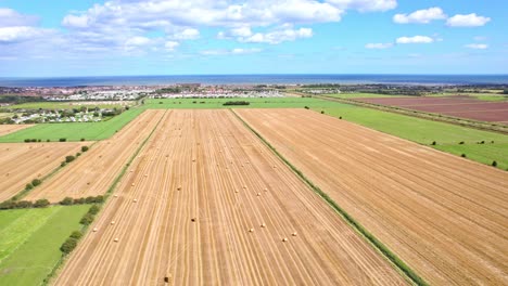Eine-Faszinierende-Luftaufnahme-Zeigt-Die-Sich-Rhythmisch-Drehenden-Windturbinen-Auf-Dem-Kürzlich-Abgeernteten-Feld-Des-Lincolnshire-Bauern,-Mit-Malerischen-Goldenen-Heuballen-Im-Vordergrund