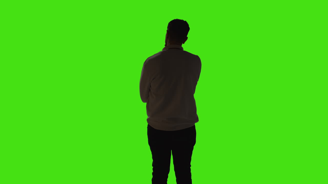 vista trasera de un joven aburrido o harto de pie y esperando con una iluminación de bajo nivel contra un fondo de pantalla verde