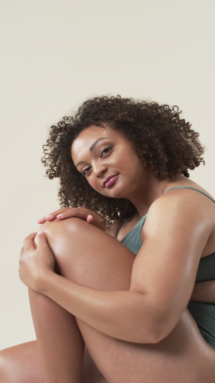 Vertical video: Smiling plus size woman embracing body positivity, sitting confidently