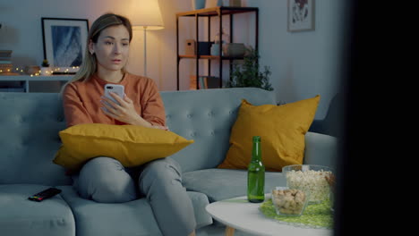 woman relaxing on sofa watching tv with smartphone