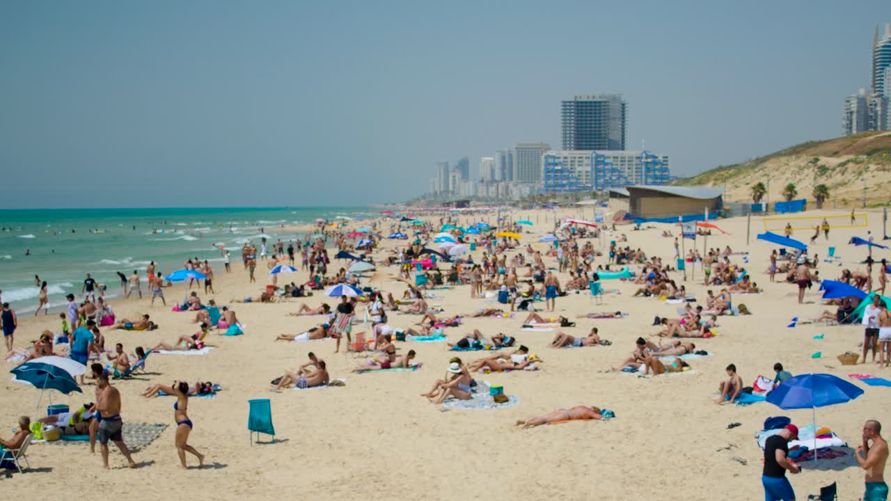 Time lapse view of the Beach showing relaxing tanning people on sand with towels and colourful umbrellas. Timelapse footage of enjoying crowed at the beach on a summer day.
