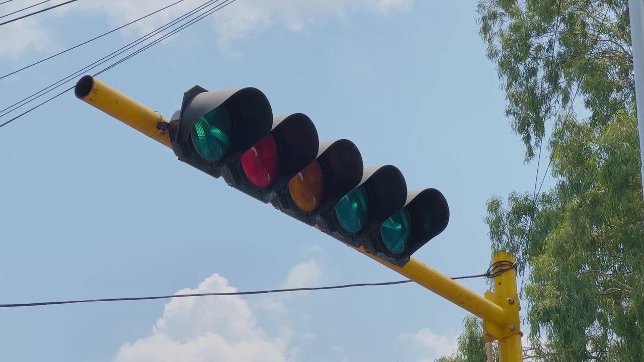 Vista de cerca de un semáforo mostrando una flecha direccional verde parpadeante con luces iluminadas contra un cielo azul, indicando el movimiento permitido de vehículos en una intersección