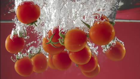 slow motion of red cherry tomatos falling into water on red background