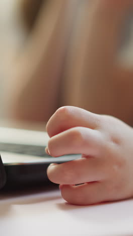 little boy hand rests near laptop. couple of classmates watches educational video sitting at desk in primary school closeup on blurred background