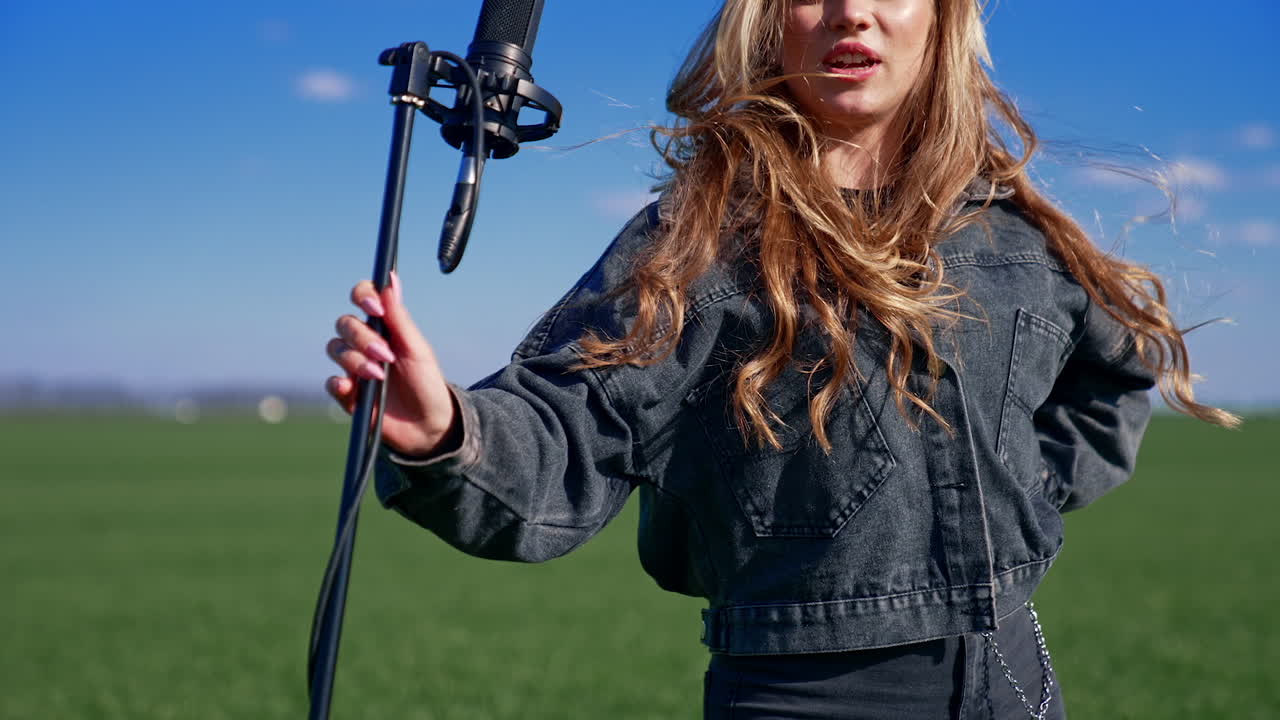 Girl singing in green field. Beautiful woman singing with microphone in green field