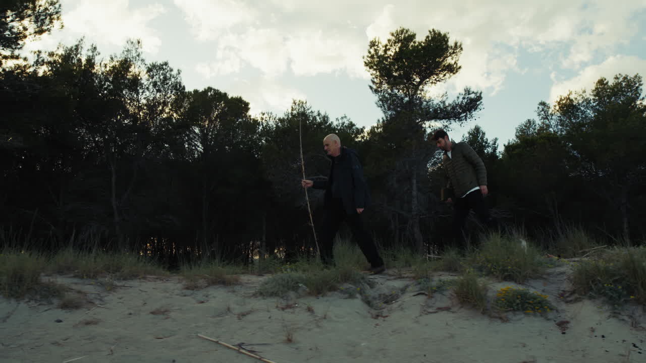 To mænd går på stranden nær fyrreskoven om vinteren ved solnedgang