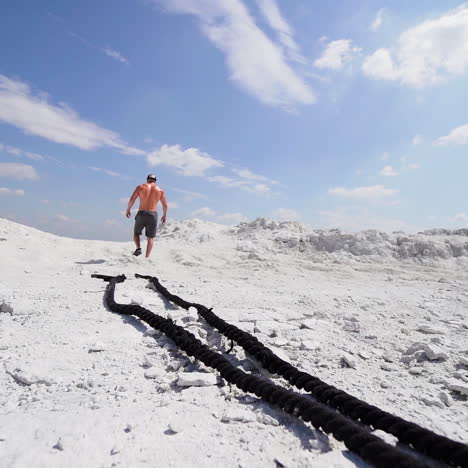 shirtless man in shorts going up after his workout with ropes outdoors. back view of a strong athlete rising on white mountain.