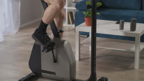 allenamento con bicicletta stazionaria a casa veduta ravvicinata delle gambe di un uomo di mezza età che gira i pedali stile di vita sano allenamento all'interno con attrezzature