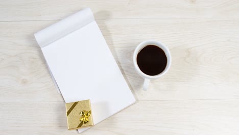 Notepad,-cup-of-coffee-and-golden-gift-box-on-wooden-surface-4k