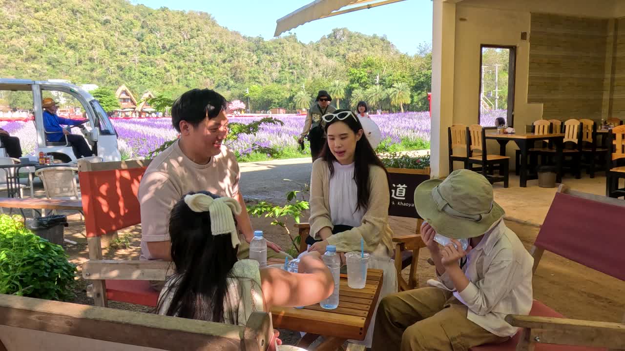 ครอบครัวสุขสันต์กำลังนั่งพูดคุยกันที่โต๊ะไม้ใกล้ทุ่งลาเวนเดอร์สีม่วง