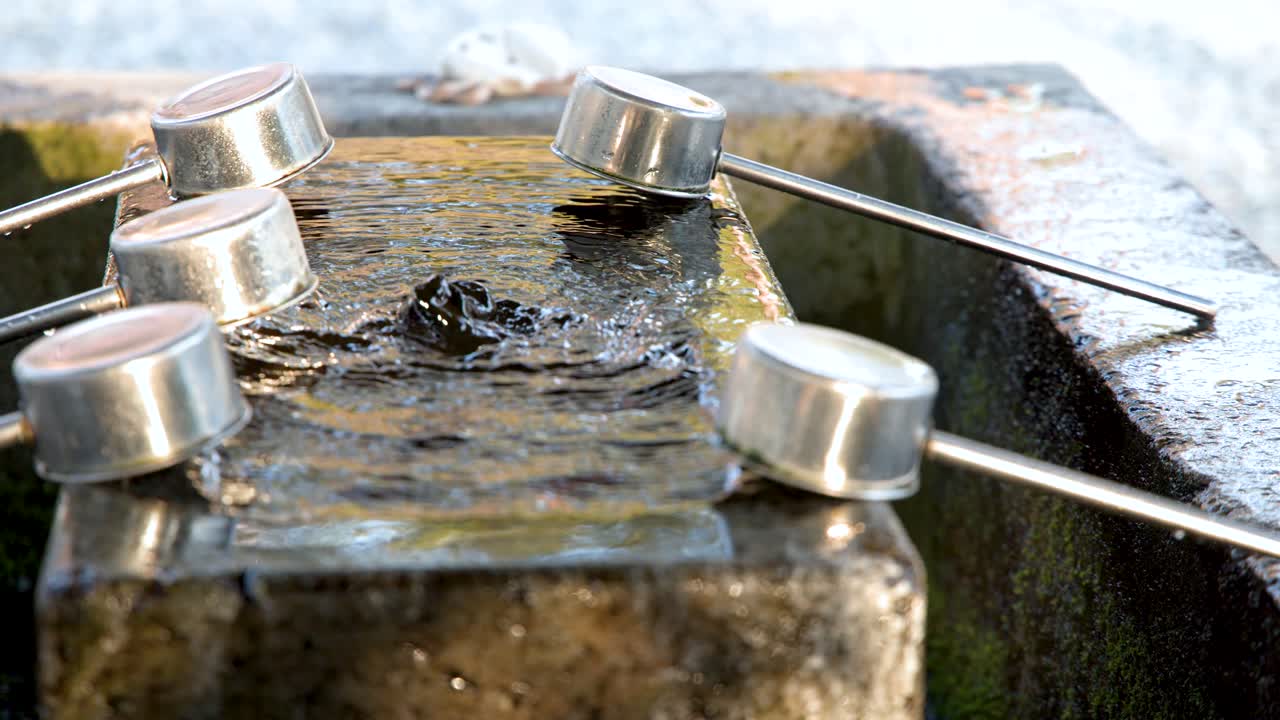 Primo piano di acqua che scorre su una vasca di pietra con mestoli di metallo in un santuario shintoista.
