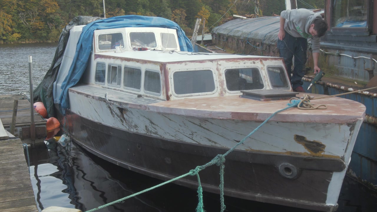 Young man repairing wooden motor cruiser drying epoxy with heat gun